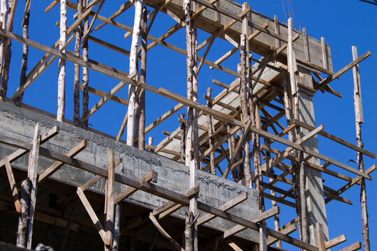 Construction site of building structure with traditional wooden bamboo scaffolding support against blue sky.