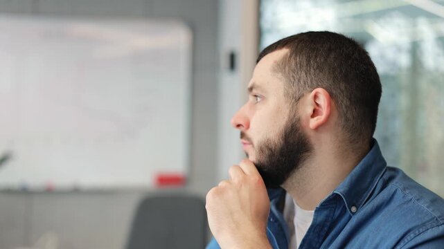 Man expresses deep contemplation, hand resting on chin, revealing focused concentration. Reflective gaze suggests serious engagement with thoughts, perhaps considering important idea or problem.