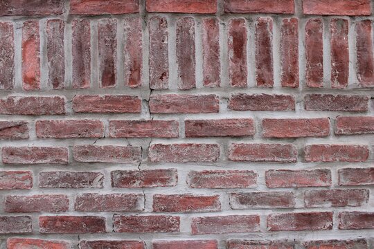 Red brick wall texture background with horizontal and vertical brick pattern, rough weathered masonry surface and gray mortar joints, rustic architectural facade detail for construction