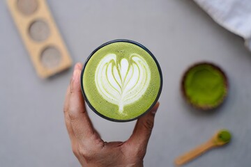 Hand Holding Matcha Latte with Intricate Art Design