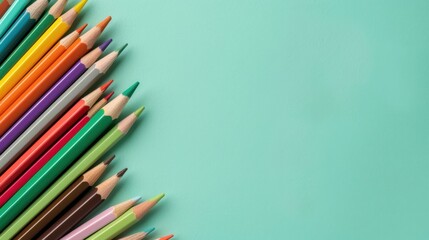 Fototapeta premium Colorful collection of vibrant colored pencils arranged on a light turquoise background displaying a creative art concept