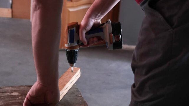 Drilling screw into wooden board. Cordless combi drill for used as drill and screw driver. Screwdriver for work with self-tapping screws in furniture workshop. Hand holding boards