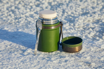 Obraz premium Green thermos for food with a spoon and a cup in winter on the snow