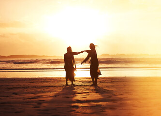 Fototapeta premium Holding hands, women and dance by sea at sunset on vacation, laughing and adventure with space. Moving, rhythm and friends at beach for holiday, summer and travel together with funny joke outdoor