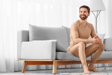 Obraz premium Handsome young man in thermal underwear sitting on sofa at home