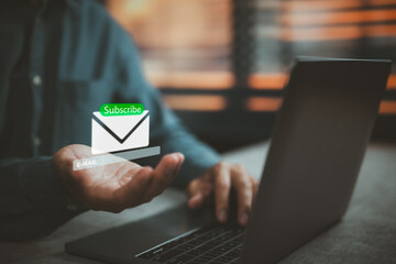 Person using laptop with holographic email subscribe icon hovering above hand