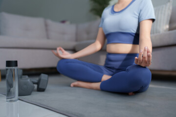 Woman meditating in lotus pose practicing yoga at home