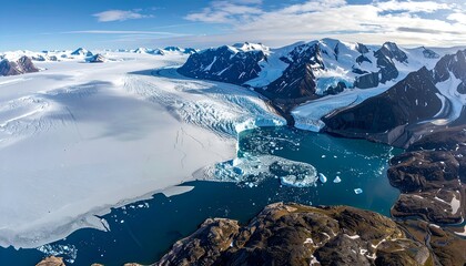 Aerial view of a glacier meeting the ocean, framed by mountains, under a blue sky