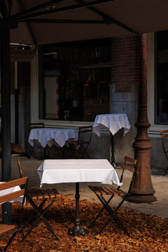 An empty terrace of a small restaurant in Amsterdam. White table cloths covering the tables.