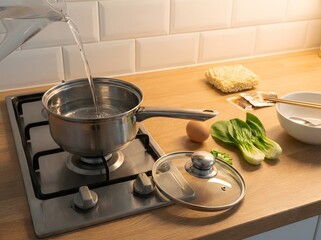 Water being poured into a stainless steel pot on a gas stove with ingredients nearby.