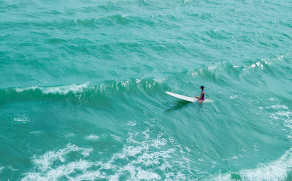 Asian play surf alone on the summer beach. Solo outdoor activity on holiday