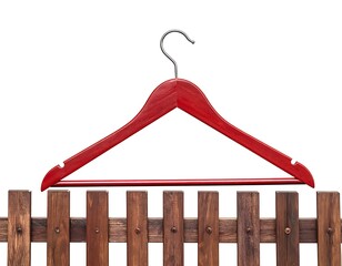 A red wooden clothes hanger rests atop a dark brown wooden fence against a stark white background