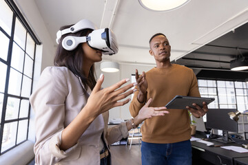 Diverse coworkers interacting with virtual reality headset, tablet at open-plan office