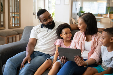 Fototapeta premium African American family sitting together and interacting with tablet on gray couch in living room