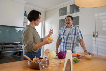 Diverse couple chopping vegetables, mixing salad in glass mixing bowl on kitchen island © wavebreak3