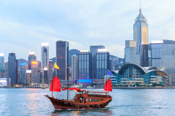 Traditional wooden junk boat with red sails against Hong Kong skyline during sunset