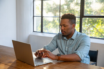 Fototapeta premium African american man typing on laptop at wooden table in office with foliage, copy space