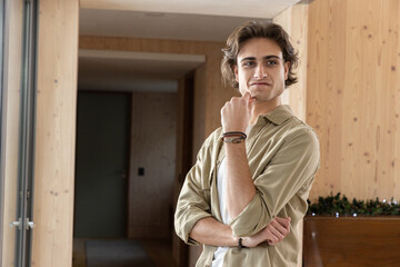 Man resting chin on wrist in wood-paneled hallway by glass sliding door with bracelets, copy space