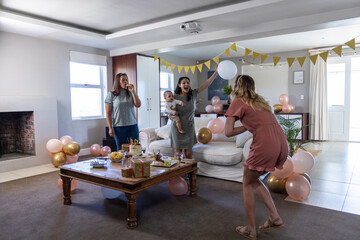 Naklejka premium Diverse women and baby boy playing around coffee table in living room with cake, balloons