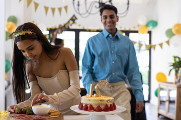 Obraz premium Asian couple celebrating birthday in dining room woman arranging charcuterie by cake, man smiling