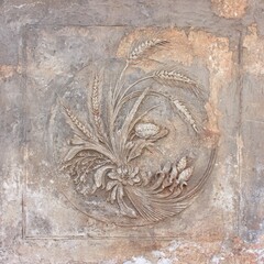 Relief carving of wheat and flowers in a circle, weathered on a stone surface