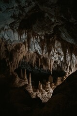 Majestic cave interior featuring dramatic stalactites and stalagmites with natural limestone formations and atmospheric shadows