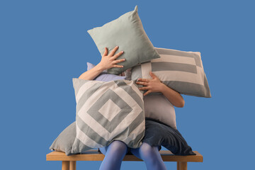 Young woman with different pillows sitting on bench against blue background