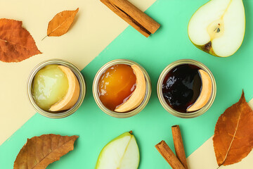 Three jars of jam on pastel yellow and green background, surrounded by pear slices, cinnamon sticks, and autumn leaves.