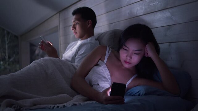 Couple in bed using smartphone, night bedroom light. Addiction social media digital technology, relationship coldness issue. Cell mobile phone scrolling problem. Useless cellphone internet surfing.