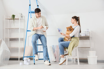 Young couple with paint and Pomeranian dog during repair in their new house