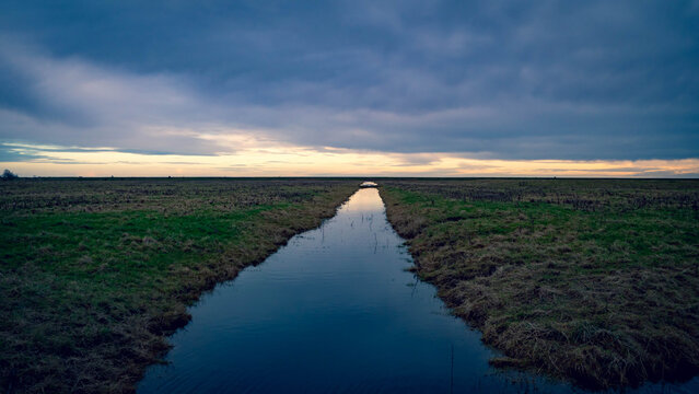 Stormy sunset at Freiston Shore, Lincolnshire with a still mirror-like dyke ditch going off to infinity point.