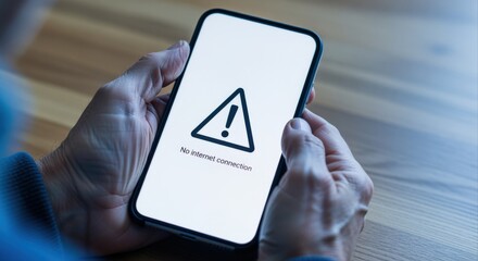 Smartphone displaying a no internet connection warning alert symbol held in hands on a wooden table