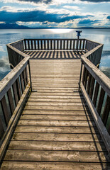 Fototapeta premium wooden pier with mountains in the distance, reflecting on calm water in the early morning light