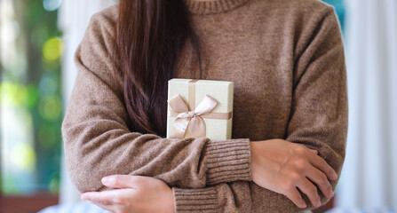 Closeup image of a woman in sweater holding a present box at home