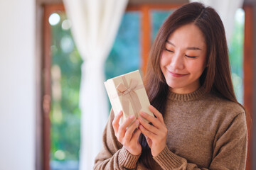 Portrait image of a woman in sweater holding and looking at a present box at home