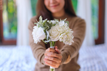 Closeup image of a woman holding and giving a white flower bouquet