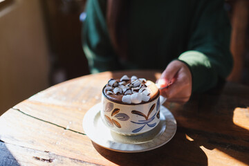 Closeup image of a woman holding a cup of hot chocolate with marshmallow on wooden table