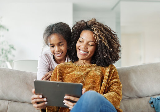 Teenage girl sitting at sofa with her mother and using tablet computer. Mother and daughter bonding and having fun at home