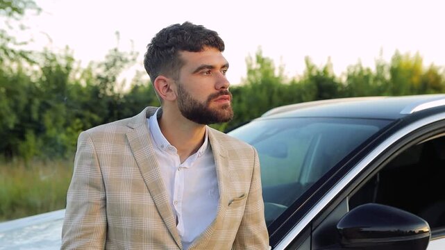 Stylish young businessman pausing during road trip, smoking cigarette near luxury vehicle while surrounded by peaceful natural landscape and enjoying personal moment of solitude


