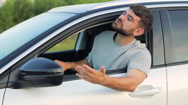 Male driver expressing road rage, yelling and making aggressive hand gestures while sitting behind steering wheel, displaying intense emotional reaction

