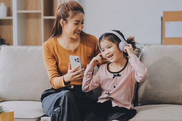A cheerful Asian mother helps her young daughter do homework and color a book at home, while the...