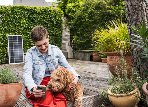 Woman enjoying time in garden with dog using mobile phone