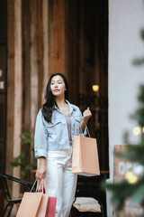 Happy Asian woman holding shopping bags outdoors in a trendy urban area, smiling confidently after shopping, representing modern lifestyle, retail experience, and consumer happiness.