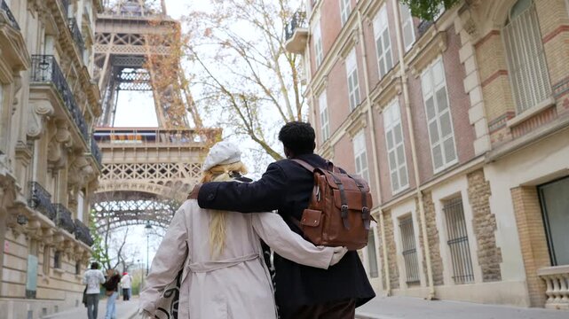 Rear view of a loving multiracial couple embracing while strolling down a picturesque parisian street, enjoying their romantic vacation together with the eiffel tower in the background