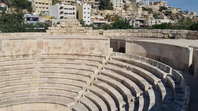 From within Amman&rsquo;s Roman Odeon Theater, ancient stone seating and well-preserved classical architecture stand in contrast to a typical hillside neighborhood under a clear blue sky and bright daylight