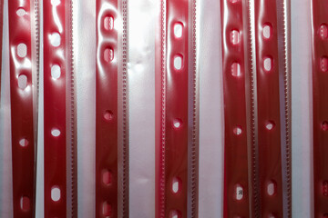 Obraz premium Vertical stripes of red plastic file pockets with perforation for document archiving arranged in a row. Abstract background of stationery supplies for organizing paper workflow in the office or at hom