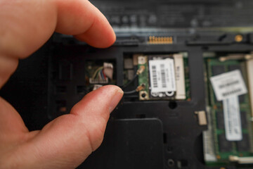 Technician's hands performing delicate work by connecting antenna cables to a Wi-Fi module inside a disassembled laptop.
