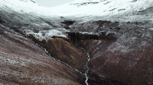 aerial shot revealing arctic alpine rivers joining and flowing down multiple waterfalls. The snow line gives way to barren reddish brown tundra rock.