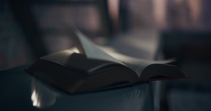 Cinematic Shot of an Open Hardcover Novel Book on a Glossy Table as a Breeze Turns Pages. Window Light and Shallow Focus Create Dreamy Bokeh, Evoking the Magic of Reading, Fiction Worlds, Learning