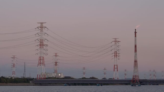 Distant view of power pylons and a lit flare stack across the water.